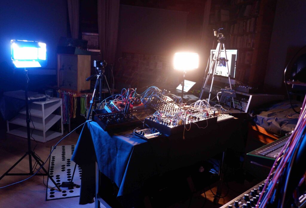 Colourful image of a music studio, with musical equipment, lights and a a table set up with music gear on it. Two strong lights create shadows