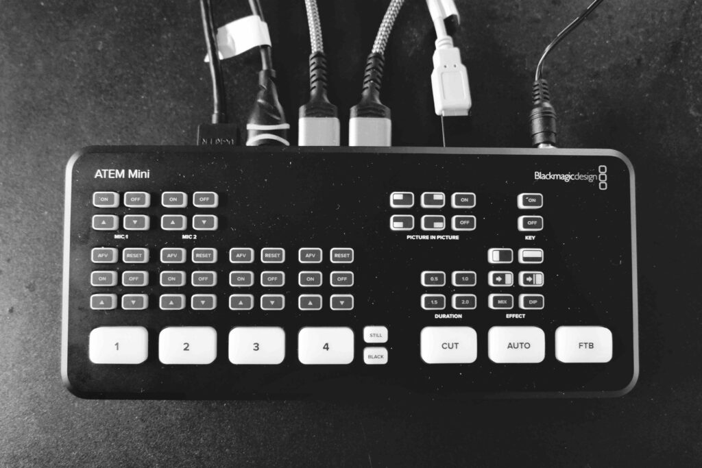 Black and white photograph of the Blackmagic Atem Mini video switcher, a table top size device. It's about the size of a large paperback boo, with white buttons over it.