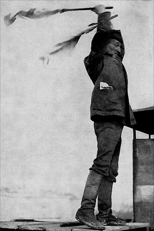 Black and white image of a Russian man in a dark suit, around 1920, waving two flags in the air in a very dramatic gesture