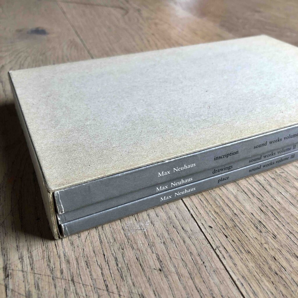 Grey books on the floor with the text Max Neuhaus on the side in white