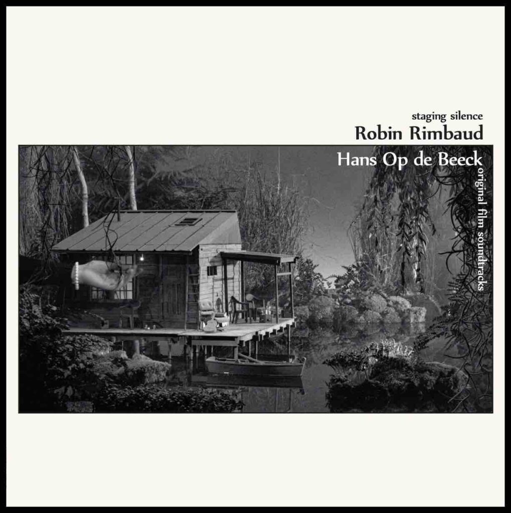 Black and white image on an LP cover, that says Robin Rimbaud Hans Op de Beeck. Image is of a house in what looks like the Amazing, foliage and trees all around, a wooden hut, water, a small boat, then you see a human hand to show the scale and realise it's a model