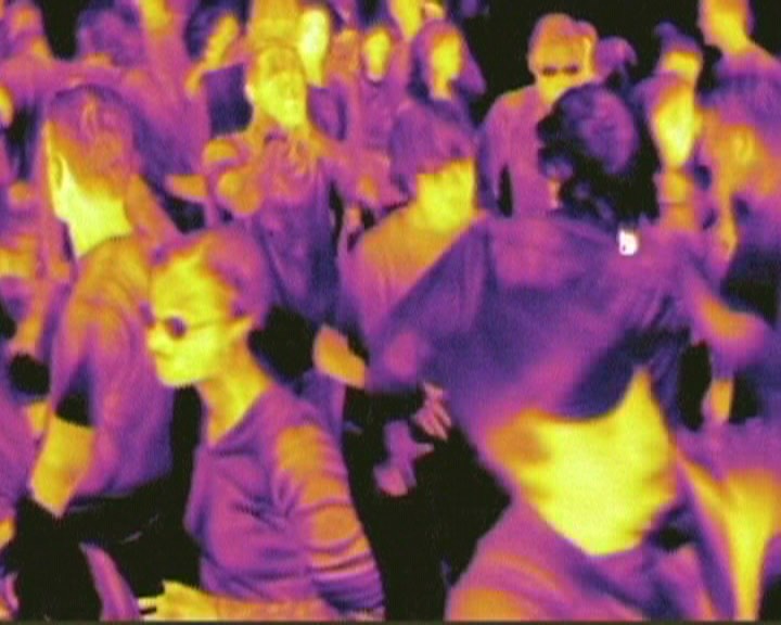 Eerie image of a crowd dancing in a nightclub but photographed with a heat sensitive camera so you only parts of their bodies are illuminated by colour