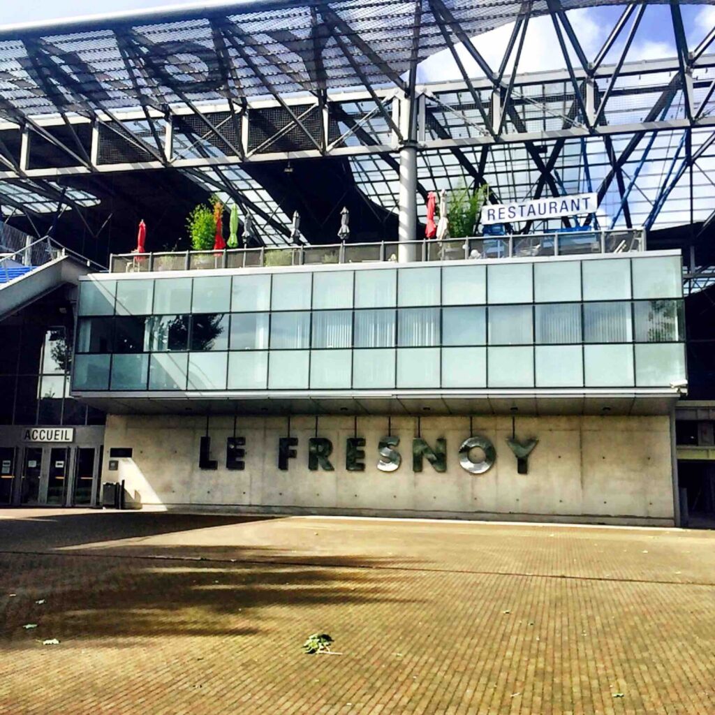 An industrial looking building with bold letters across it - LE FRESNOY, with huge open plan architecture. No people visible