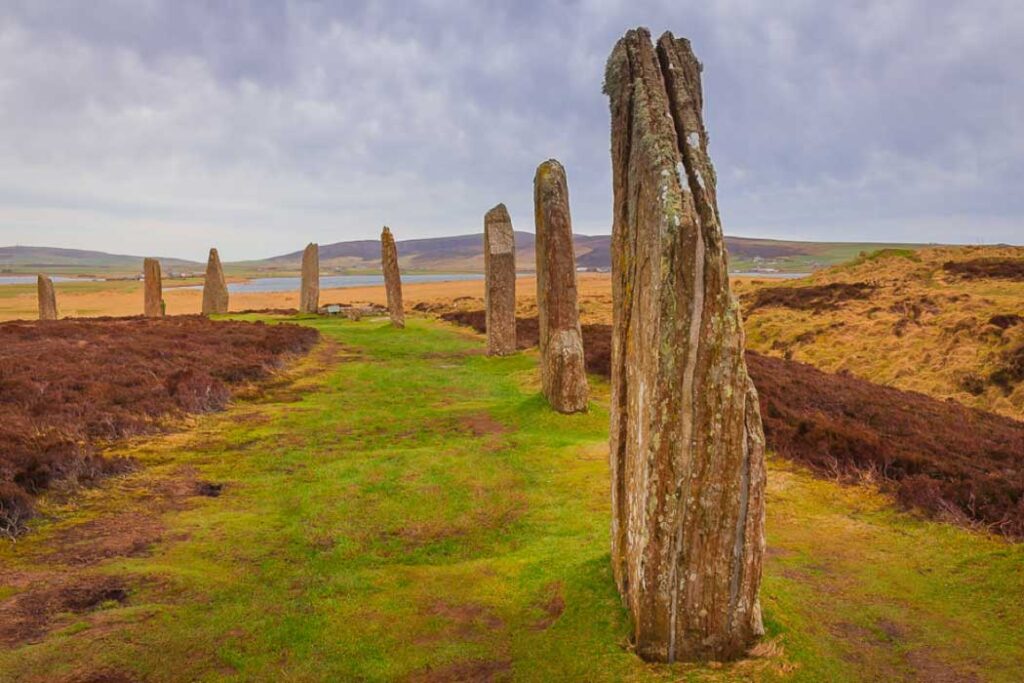 You see a series of ancient stones set up in a line across a photo of a remote landscape in colour