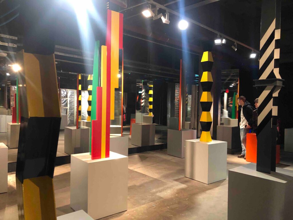 Colourful sculptures in columns, with lines and strips of colour all around them in a gallery space