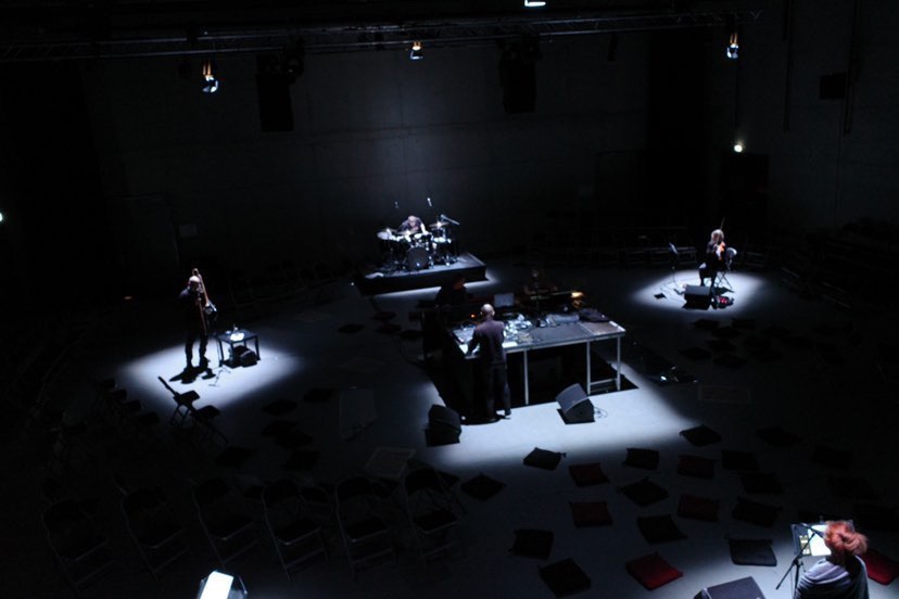 Dramatic overview photo of 5 musicians on stage, lit very dramatically from above