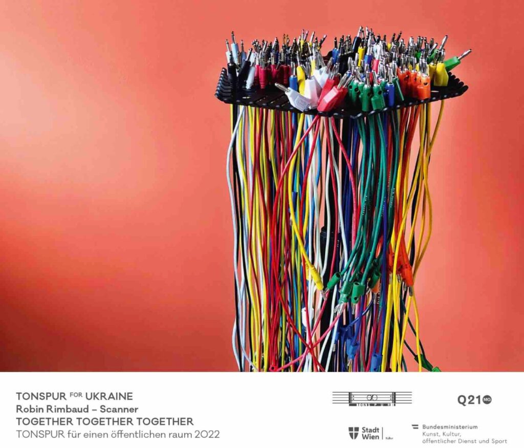Colourful image of a postcard, featuring a photo of a large group of mixed coloured electronic cables hanging from a stand, in front of an orange wall 