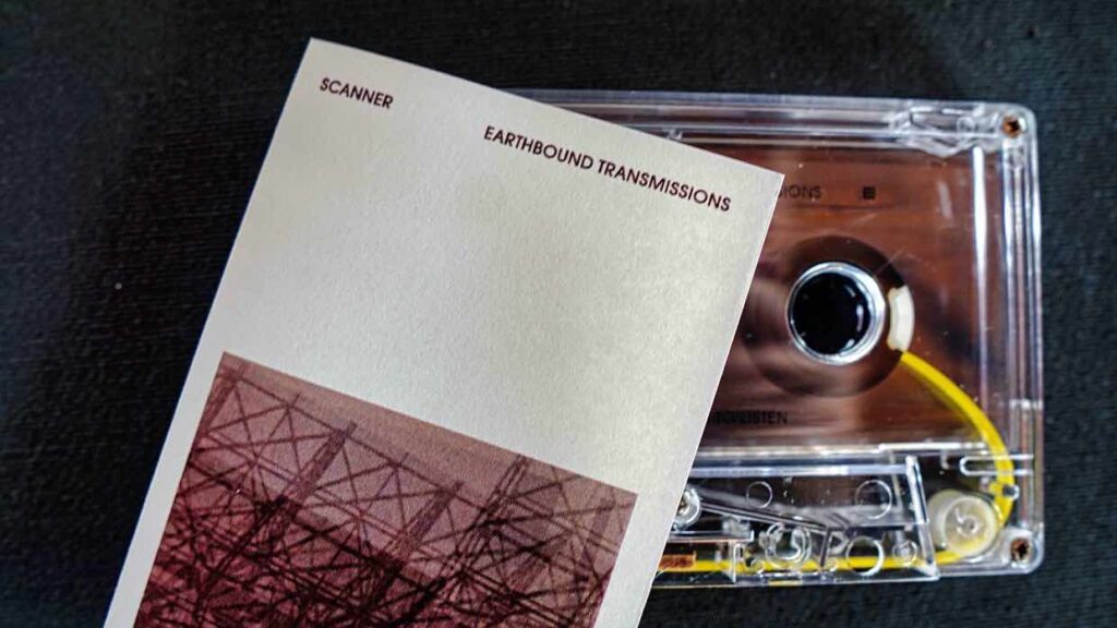 A cassette and cover for the tape, with the words Scanner - Earthbound Transmissions on the artwork. Colours are a deep faded purple.