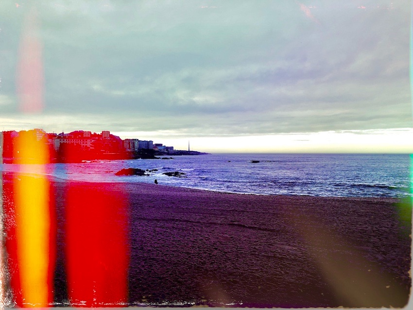 Colourful photograph of the sea at A Coruna in Spain, with light leaking into the image from the left side, creating bright red and yellow streaks of colour