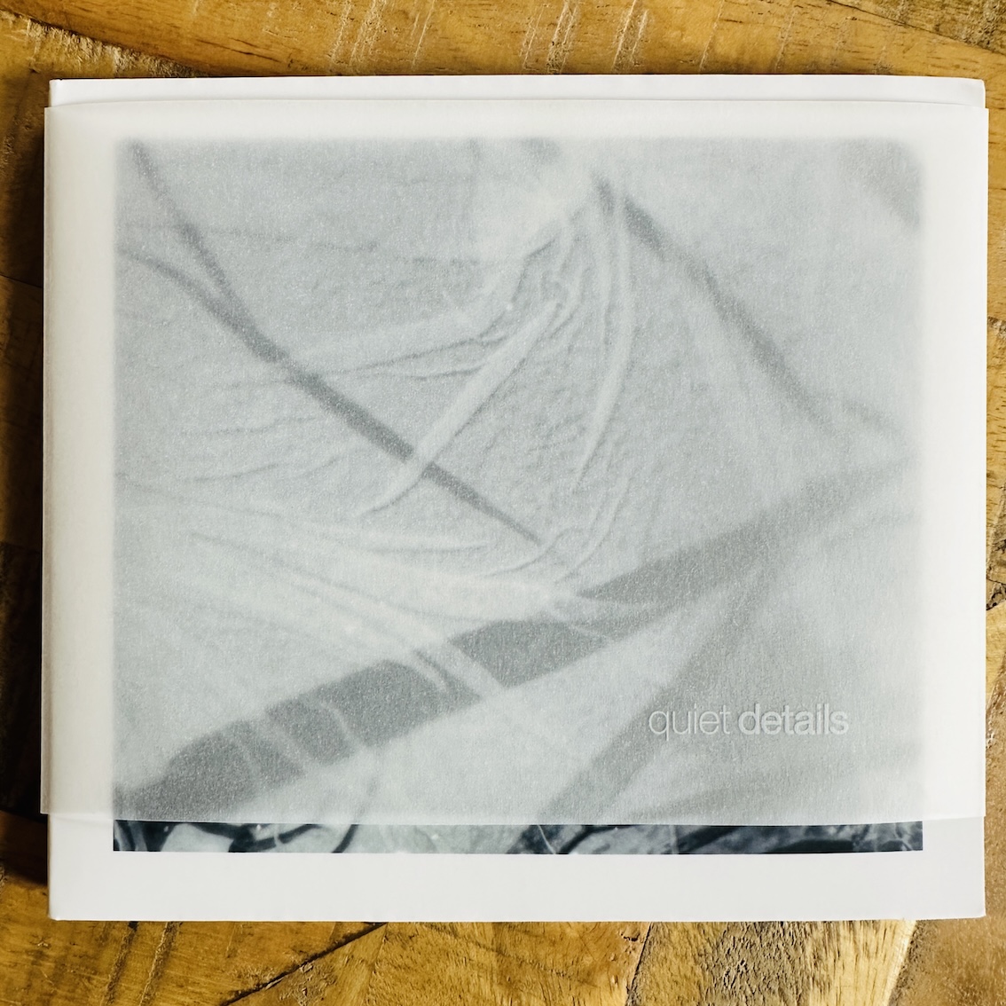 Album artwork with a grey abstract image hidden beneath a piece of transparent paper with the name Quiet Details printed on it