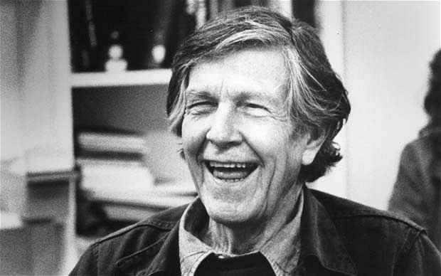 An older white man, John Cage, in black and white, seen from the shoulders up laughing