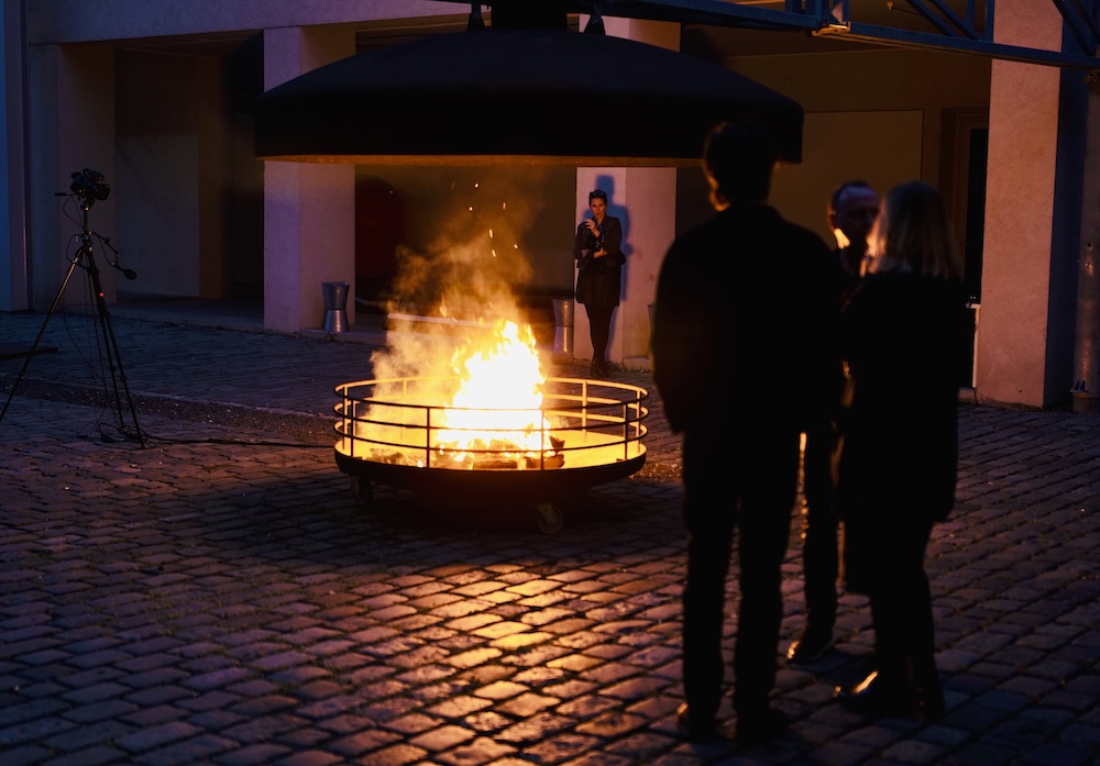 Figures stand outdoors around an open fire in a courtyard