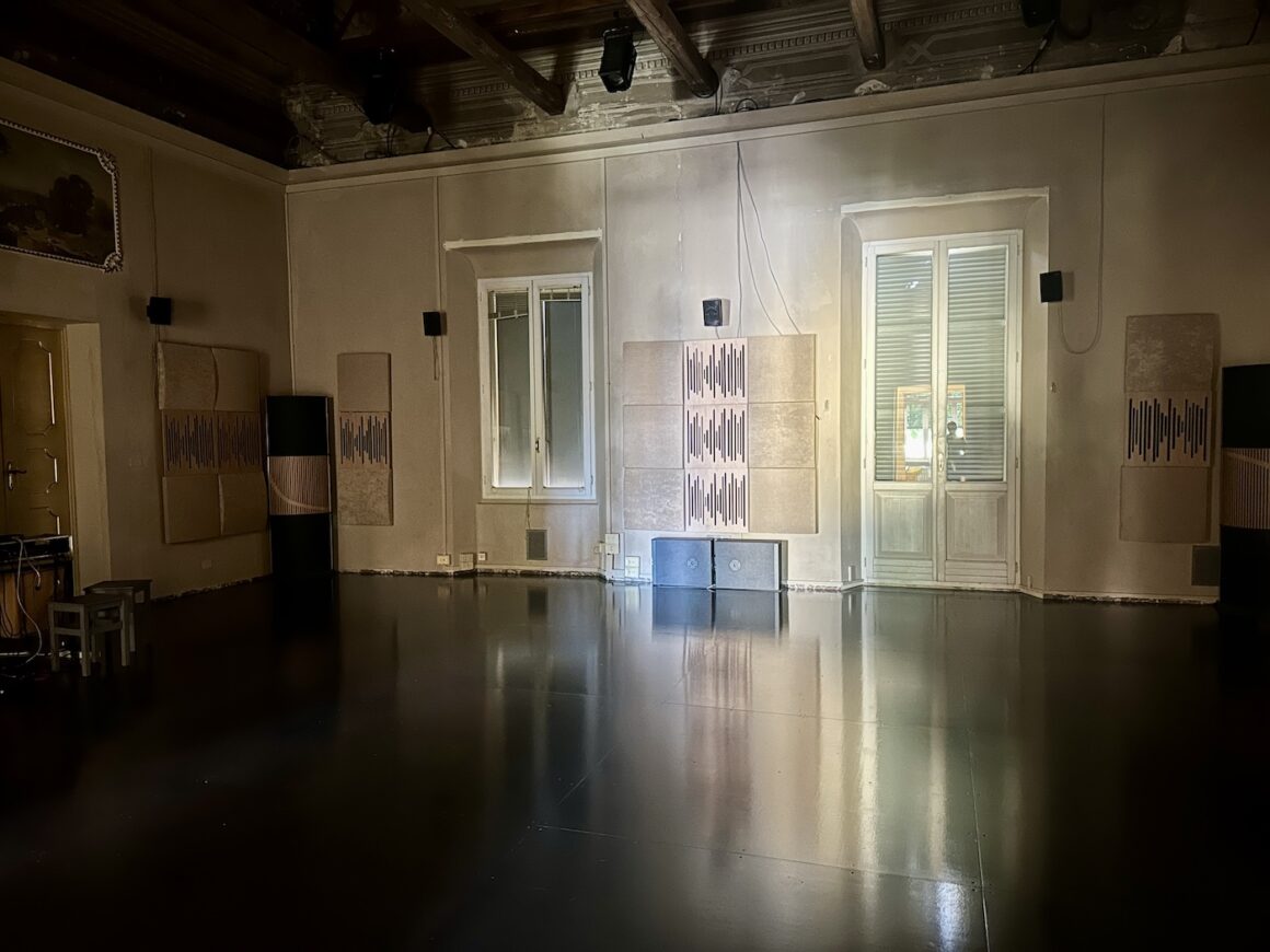 Empty rehearsal or dance studio room with wooden ceiling beams, large windows, soundproof panels on the walls, and polished dark floor.
