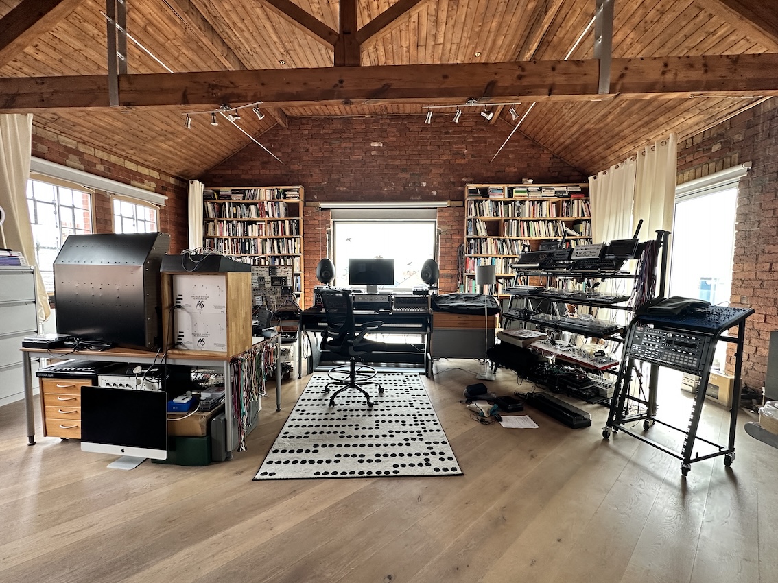 A music studio in a large open light wooden space Musical equipment is set up in the central space, with a smart carpet in the middle. Large wooden beams hang overhead